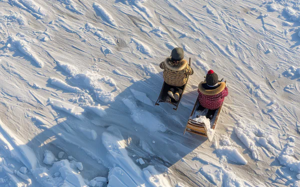 Two people enjoy sledding down a snowy hill, captured in a high-definition desktop wallpaper with clear sled tracks and winter atmosphere.