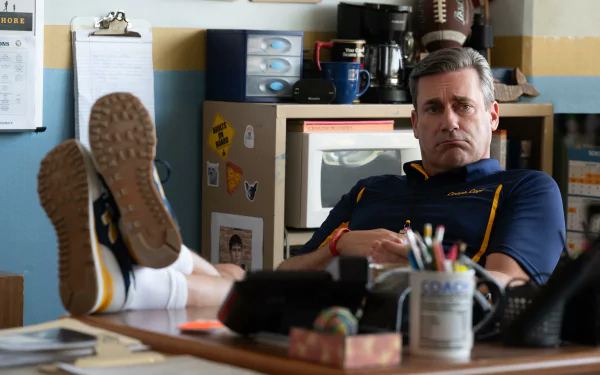 HD desktop wallpaper featuring a scene from Mean Girls (2024) with a character lounging with feet up on a desk, set in an office environment.