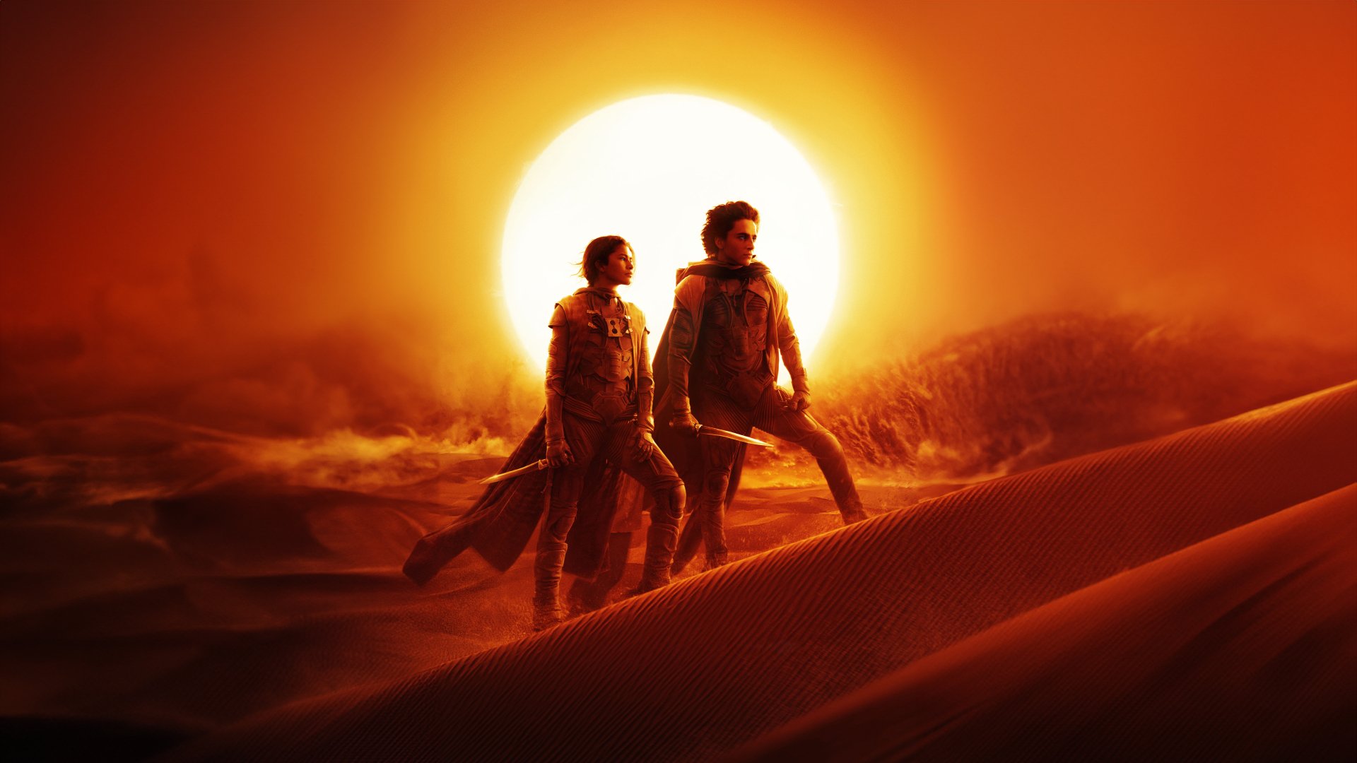HD desktop wallpaper featuring two characters from Dune: Part Two walking in a desert landscape with a looming sun in the background, symbolizing the epic sci-fi saga.