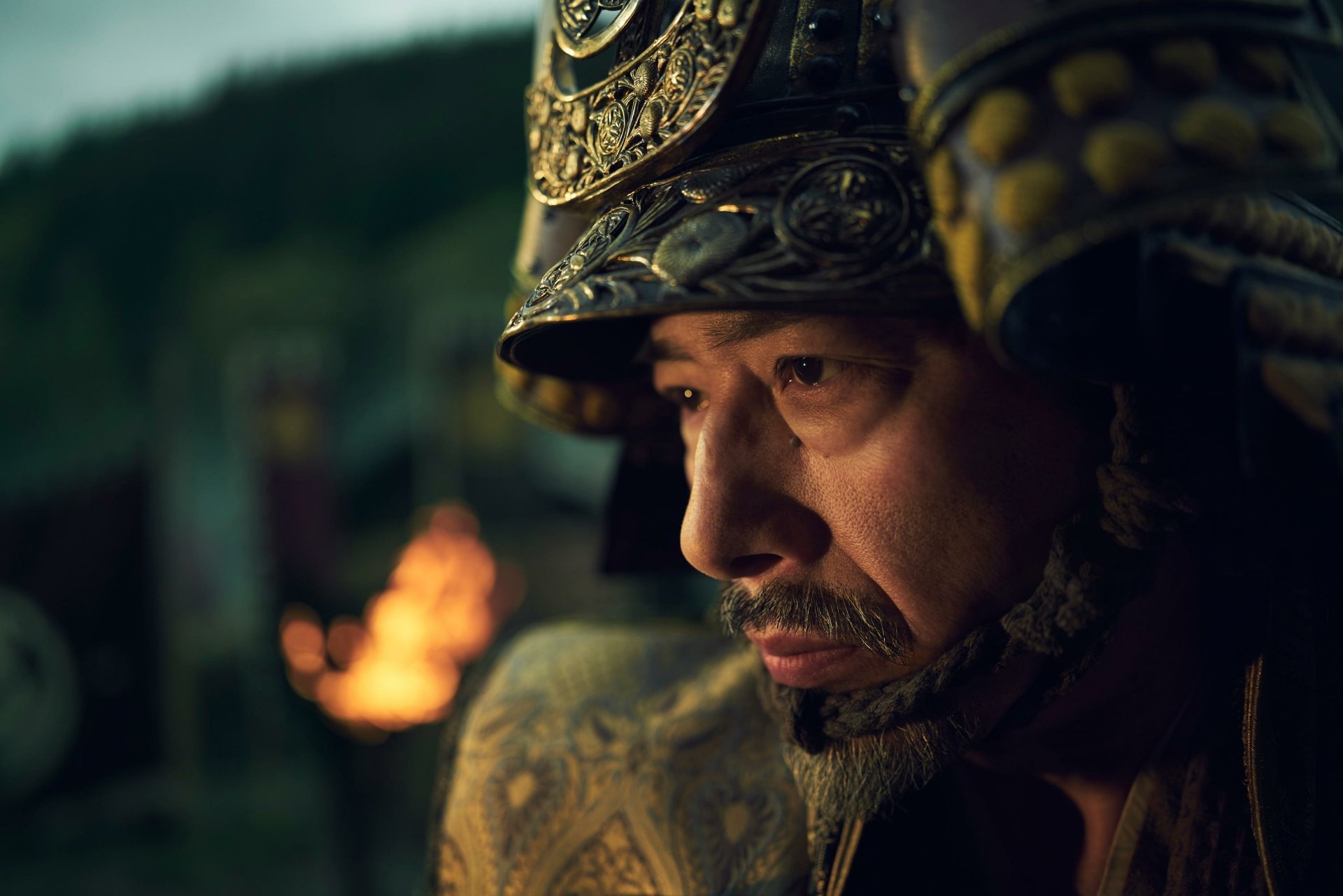 HD wallpaper featuring a close-up of a character in traditional samurai armor from the 2024 TV show Shogun, with a contemplative expression and a blurred torchlit background.