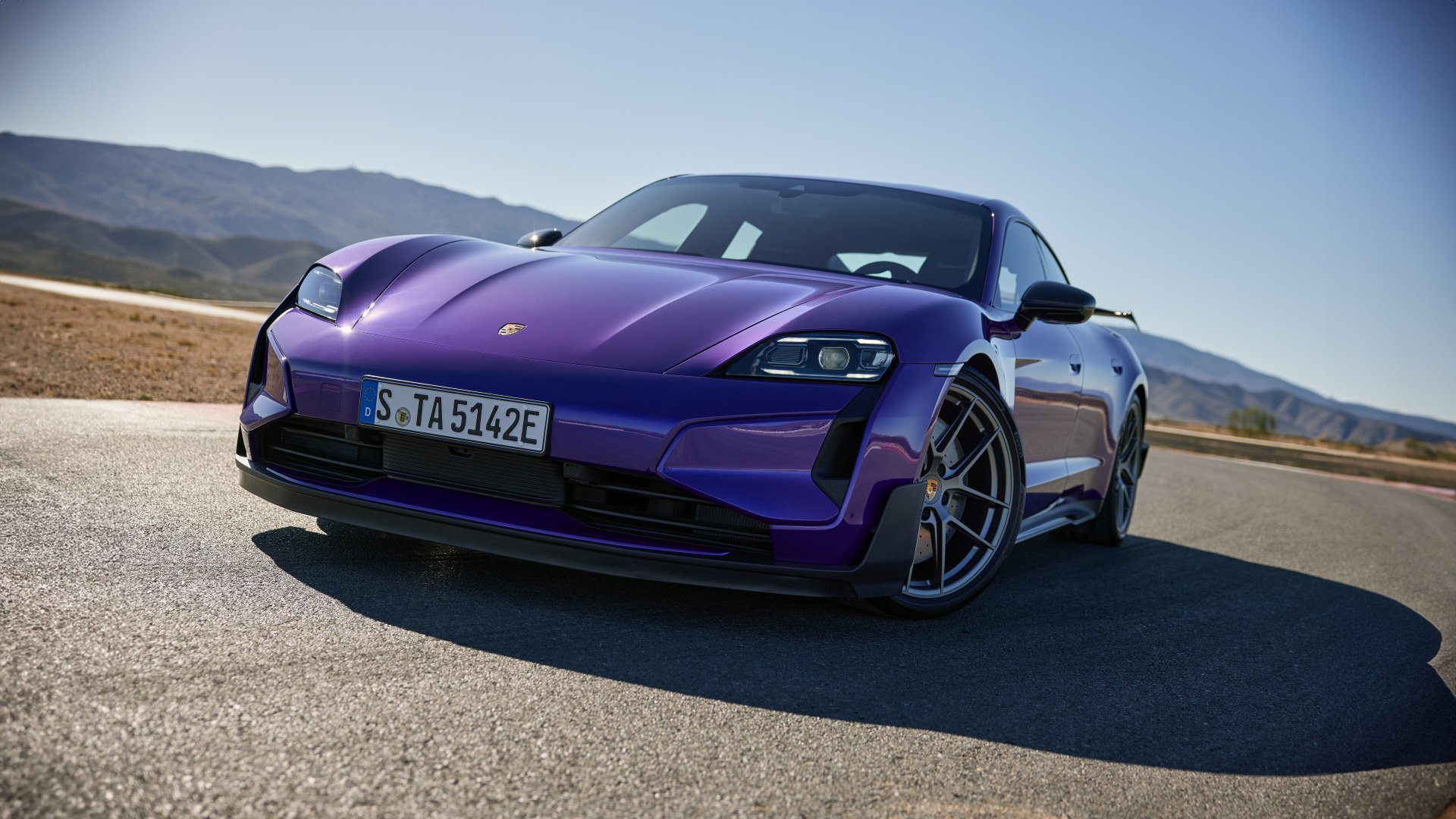A striking Porsche Taycan Turbo S in vibrant purple parked on a scenic road, showcasing its elegant design and performance capabilities. An eye-catching HD wallpaper for car enthusiasts.