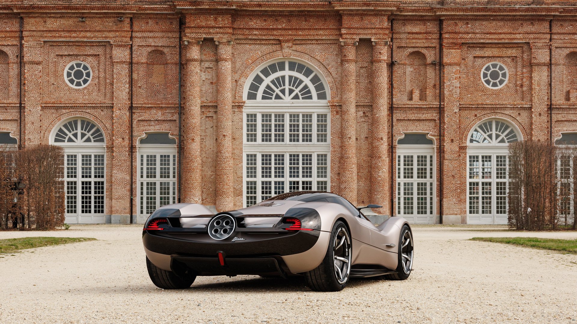 A Pagani Huayra parked in front of an elegant brick building with large windows and arching doorways, suitable as a high-definition desktop wallpaper and background.