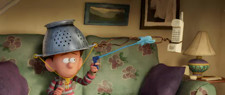 HD wallpaper featuring an animated character from the movie 'Orion and the Dark' wearing a colander as a helmet and holding a slingshot, with a cozy room background.