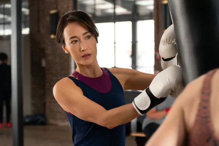 HD desktop wallpaper from the movie The Family Plan featuring a person boxing with a punchbag in a gym.