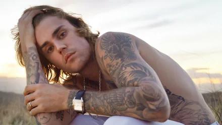 HD desktop wallpaper featuring a contemplative person with prominent tattoos sitting outdoors, associated with music.