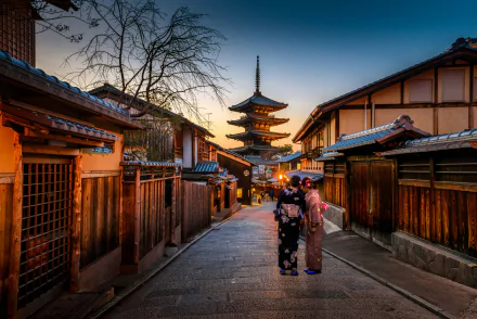 A serene Kyoto street at sunset, featuring traditional wooden buildings and a pagoda. Two women in colorful kimonos add cultural charm to this stunning Japanese temple backdrop.