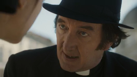 HD wallpaper featuring a scene from the movie 'The First Omen' with a close-up of a character dressed as a priest wearing a blue hat.