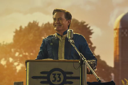 A person standing at a podium with a microphone, featuring the number 33 and the symbol of an atom, with a warm sunset and industrial structures in the background, as an HD wallpaper for the Fallout TV show.