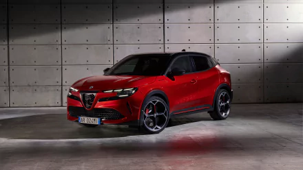 A red Alfa Romeo Milano Veloce parked in front of a grey concrete wall, serving as an HD desktop wallpaper and background.