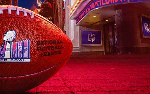 Close-up of an American football with the Super Bowl and NFL logos, set against a vibrant background with stadium lights, perfect for a sports-themed HD desktop wallpaper.