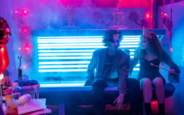 A vibrant scene from the movie Lisa Frankenstein, featuring two characters sitting on a glowing blue bench amidst colorful smoke and eclectic decor, designed as an HD desktop wallpaper.