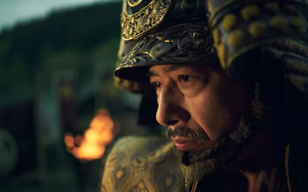 HD wallpaper featuring a close-up of a character in traditional samurai armor from the 2024 TV show Shogun, with a contemplative expression and a blurred torchlit background.