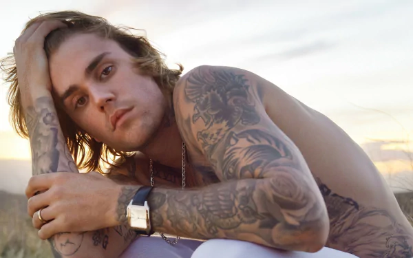 HD desktop wallpaper featuring a contemplative person with prominent tattoos sitting outdoors, associated with music.