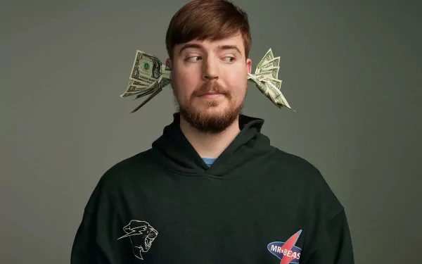 Man in hoodie with money behind ears posing for an HD Mr. Beast themed desktop wallpaper background.