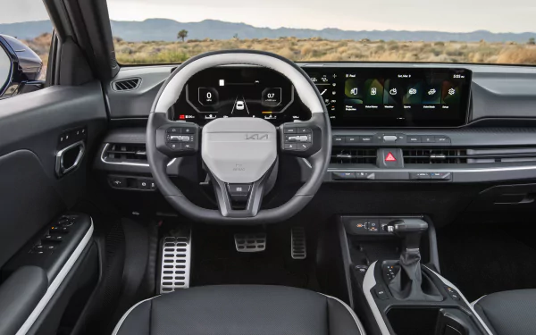 Interior view of a Kia K4 GT-Line, showcasing a modern dashboard, touchscreen display, and sporty steering wheel, featuring a sleek design against a scenic background.