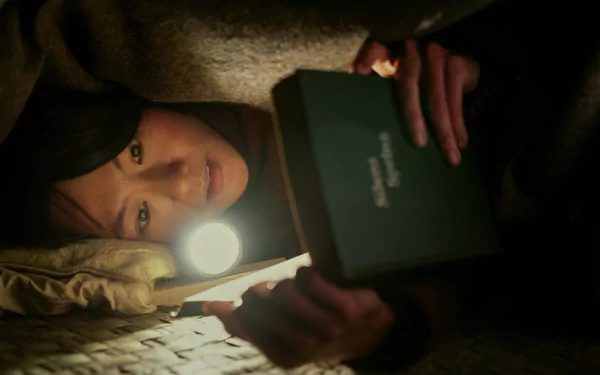 A person under a blanket with a book titled '3-Body Problem' illuminated by flashlight — HD wallpaper from the TV show adaptation.