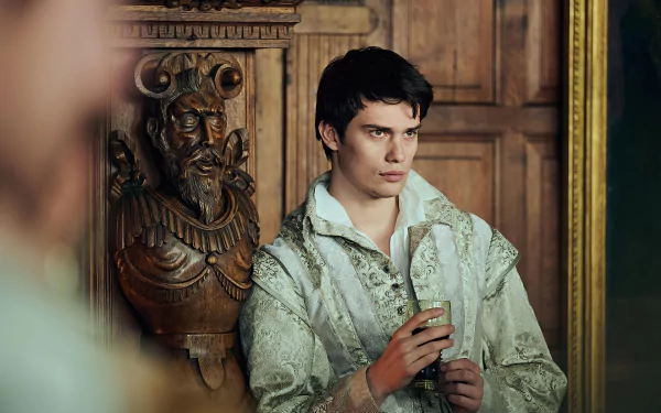 Nicholas Galitzine portraying a character from the TV show Mary & George in a high-definition wallpaper, featuring a close-up in vintage attire set against a historical wooden backdrop.