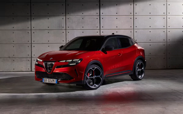 A red Alfa Romeo Milano Veloce parked in front of a grey concrete wall, serving as an HD desktop wallpaper and background.
