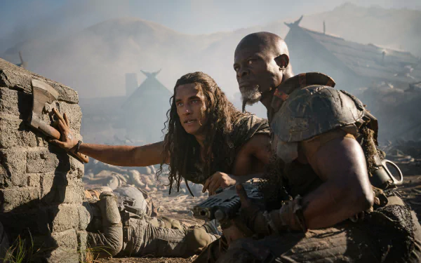 HD wallpaper featuring two characters from the movie 'Rebel Moon - Part Two: The Scargiver' crouching behind rubble with tense expressions, hinting at a dramatic moment in a desolate, war-torn setting.