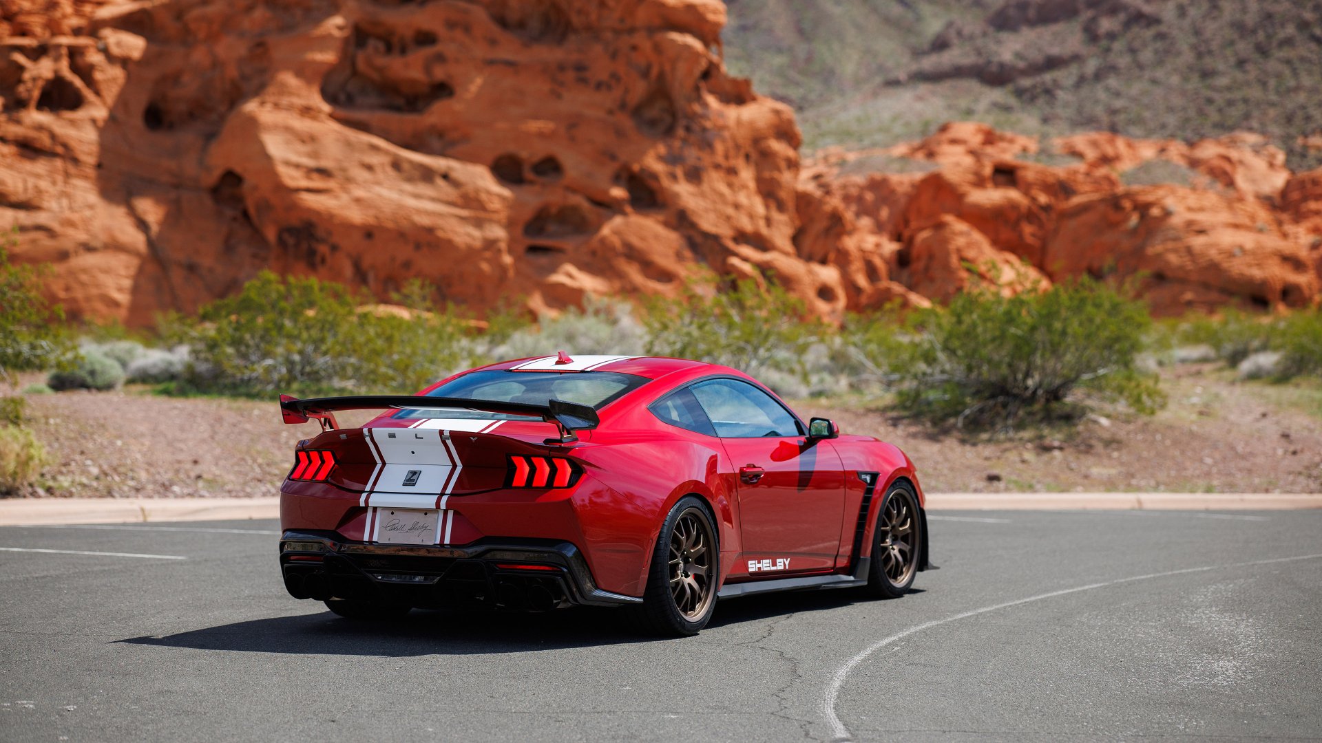 HD desktop wallpaper of a red Shelby Super Snake muscle car parked on a desert road against a backdrop of rocky terrain.