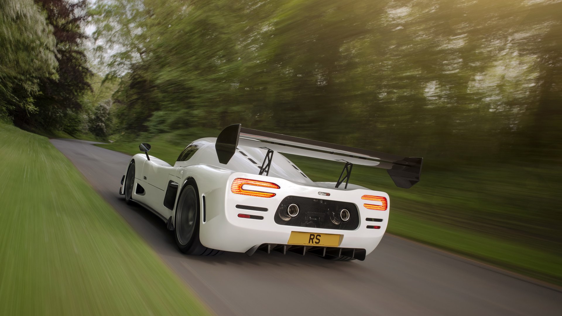 HD desktop wallpaper of a white Ultima RS speeding along a lush, green roadside.