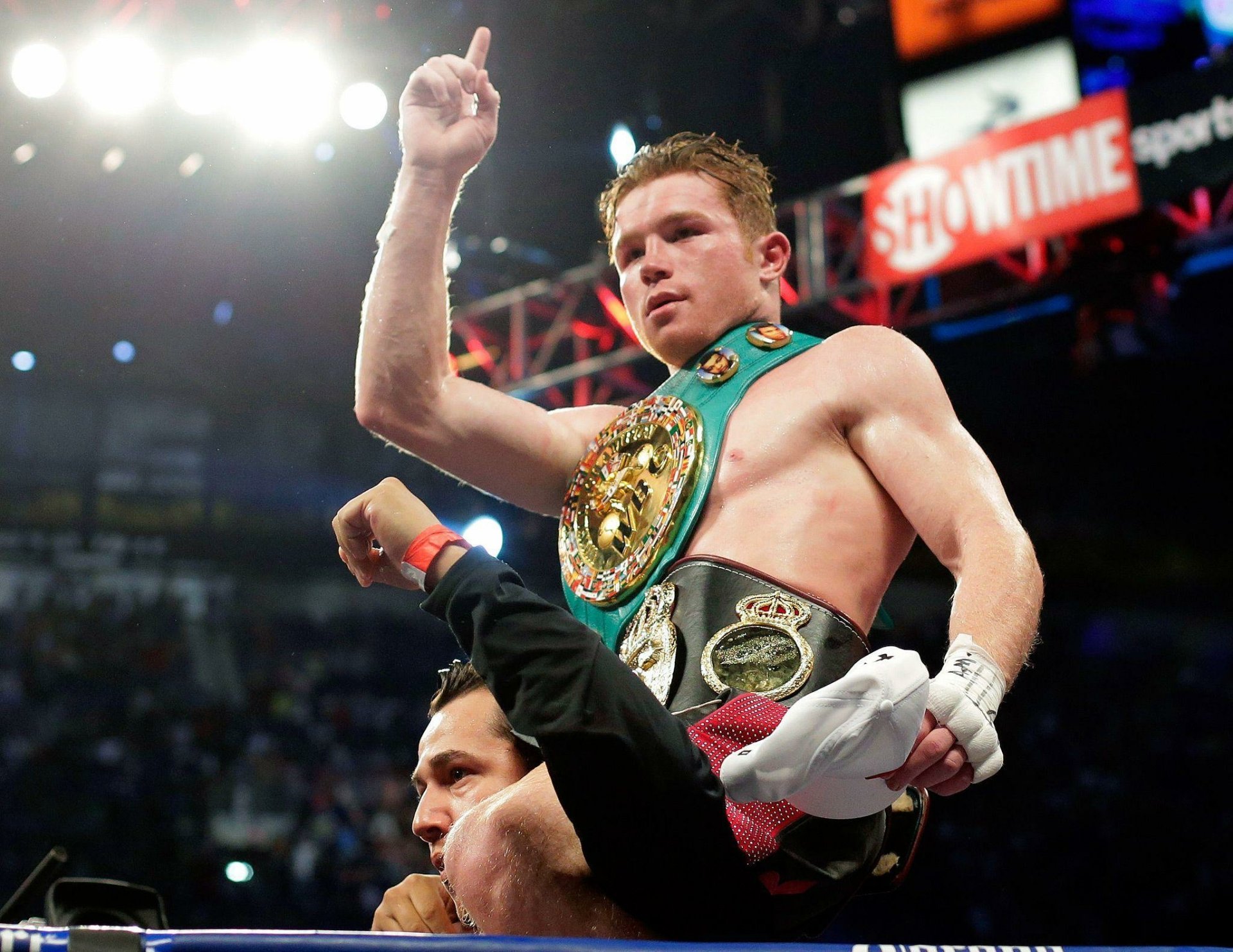 HD wallpaper of boxer Canelo Álvarez celebrating a victory in the ring, lifted triumphantly with a championship belt.