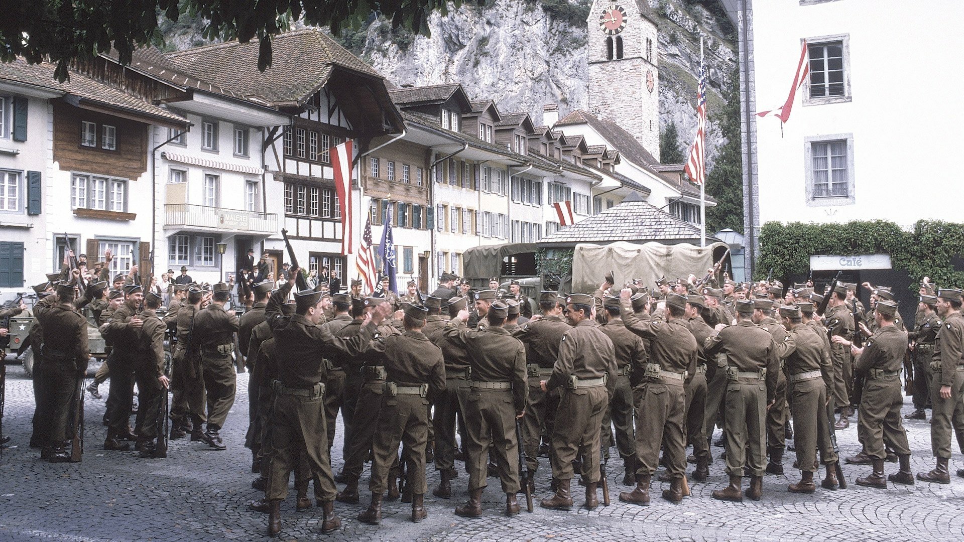 HD desktop wallpaper from the TV show Band of Brothers depicting a large gathering of soldiers in uniform in a European town square.