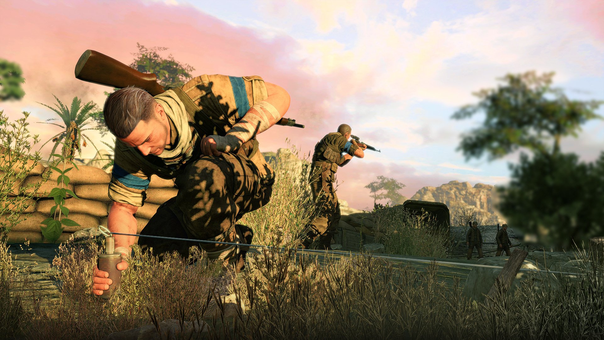 HD desktop wallpaper featuring a scene from the video game Sniper Elite III. Two soldiers are crouched, aiming with rifles amidst a rugged landscape under a pink-tinged sky.