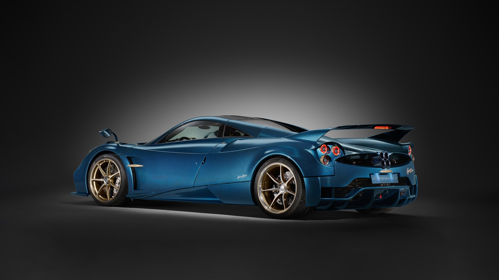 HD wallpaper featuring a sleek, blue Pagani Huayra Epitome car with golden rims, against a dark gradient background.