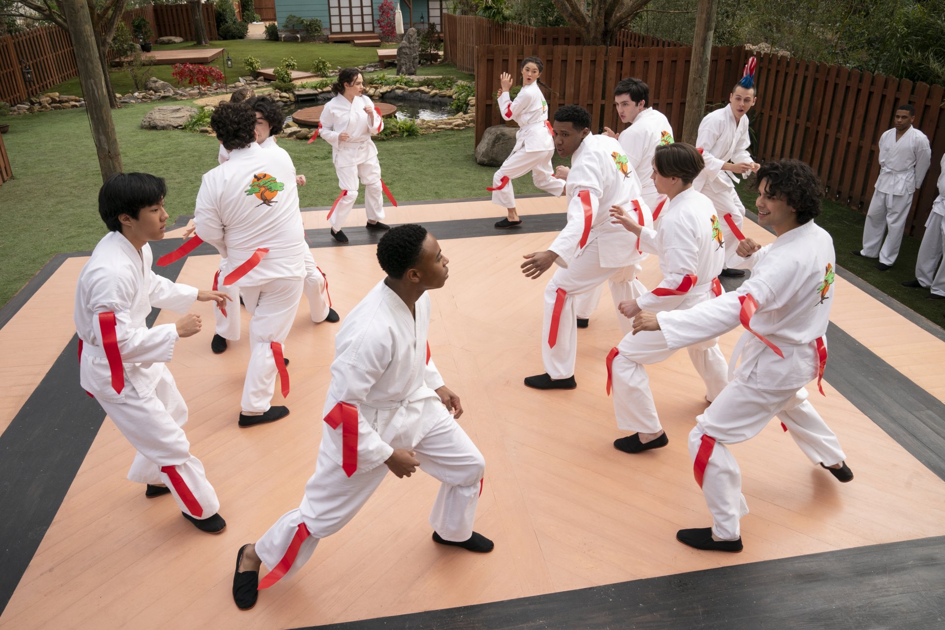A HD desktop wallpaper from the TV show Cobra Kai, featuring multiple characters in karate uniforms practicing martial arts in an outdoor setting.