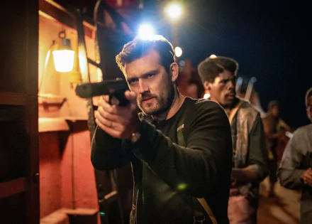 HD wallpaper of a scene from a movie with a man in the foreground aiming a weapon, intense expression on his face, another person in the background, and dimly lit surroundings suggesting a tense moment.