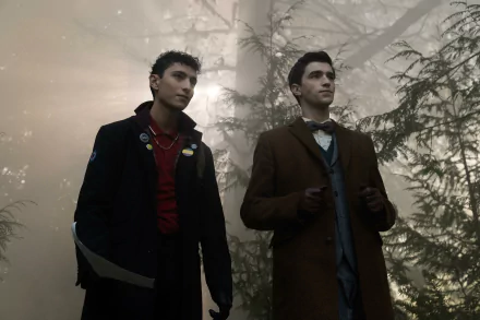 HD wallpaper from the TV show Dead Boy Detectives featuring two young men in a misty forest, dressed in dark and formal outfits.