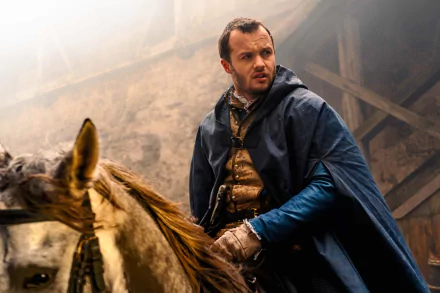 HD wallpaper of a scene from the TV show Shardlake, featuring a man in historical attire beside a horse in a foggy stable setting.