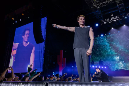 HD wallpaper of Nicholas Galitzine performing on stage in a scene from the movie The Idea of You, with a cheering crowd and vibrant stage effects.