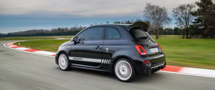 HD desktop wallpaper featuring a sleek black Fiat Abarth 695 Esseesse speeding on a racetrack, showcasing its sporty design against a blurred background of green fields and trees.