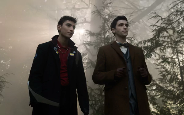 HD wallpaper from the TV show Dead Boy Detectives featuring two young men in a misty forest, dressed in dark and formal outfits.