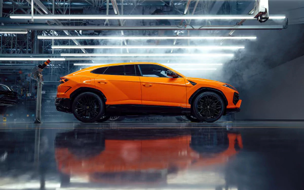 HD wallpaper of a bright orange Lamborghini Urus parked in a sleek, industrial garage, emitting a dynamic and luxurious vibe.