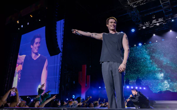 HD wallpaper of Nicholas Galitzine performing on stage in a scene from the movie The Idea of You, with a cheering crowd and vibrant stage effects.