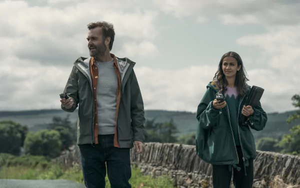 HD desktop wallpaper from the TV show Bodkin featuring Will Forte and a female co-star walking with remote controls in a rural setting.