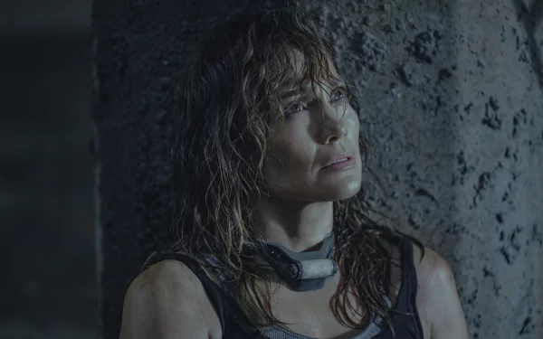 A HD desktop wallpaper featuring a scene from Atlas (2024), showing a determined woman with wet hair leaning against a weathered stone wall.