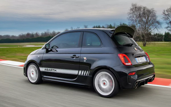 HD desktop wallpaper featuring a sleek black Fiat Abarth 695 Esseesse speeding on a racetrack, showcasing its sporty design against a blurred background of green fields and trees.