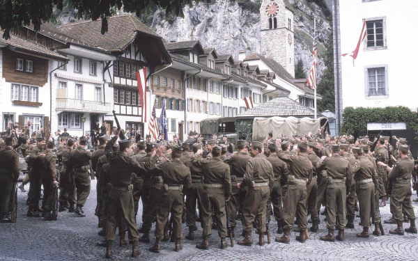 HD desktop wallpaper from the TV show Band of Brothers depicting a large gathering of soldiers in uniform in a European town square.