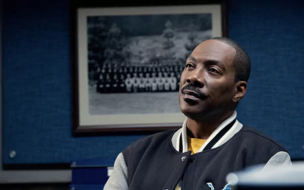 HD wallpaper of Eddie Murphy in Beverly Hills Cop: Axel F, featuring him in a thoughtful pose against a blue background with a framed photo behind him.
