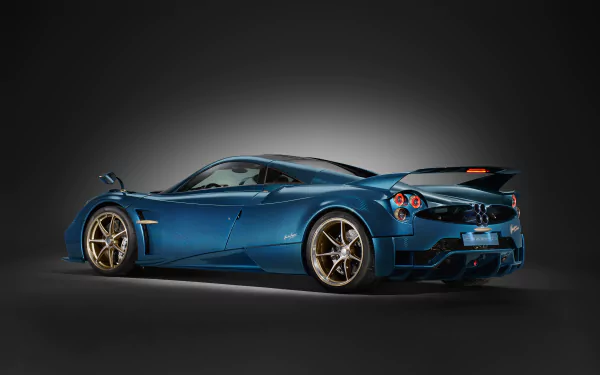 HD wallpaper featuring a sleek, blue Pagani Huayra Epitome car with golden rims, against a dark gradient background.