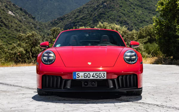 A HD desktop wallpaper featuring the front view of a striking red Porsche 911 Targa 4 GTS, set against a backdrop of mountains and greenery.
