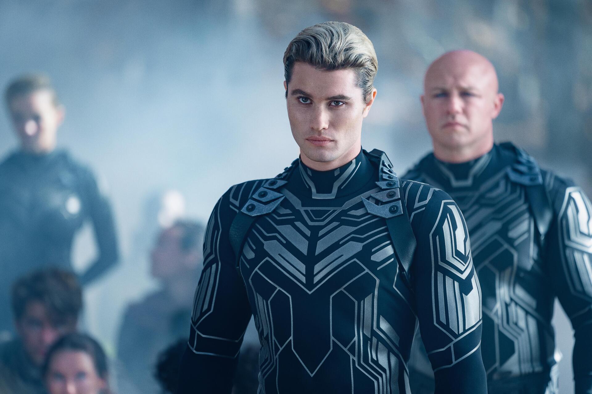 A close-up of Chase Stokes in a futuristic outfit, surrounded by others in a misty setting, from the movie Uglies. High-resolution wallpaper showcasing a dramatic scene.