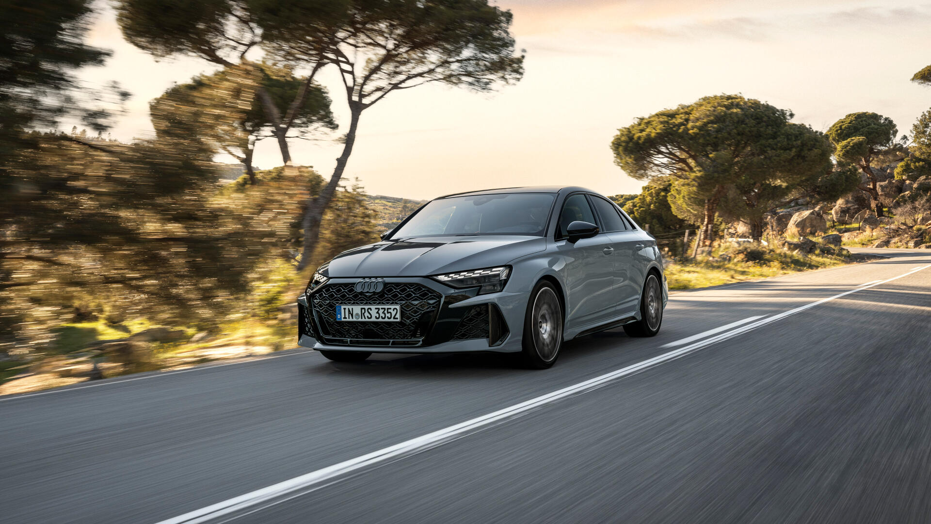 A sleek Audi RS3 Sedan in motion on a scenic road, surrounded by trees, captured in stunning 4K Ultra HD detail for a striking desktop wallpaper.