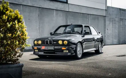 A sleek black BMW E30 M3 parked against a modern backdrop, showcasing its iconic design. This HD wallpaper captures the essence of automotive performance and style.