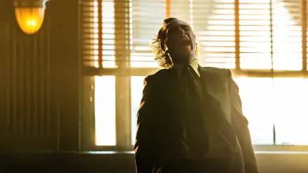 Joaquin Phoenix as the Joker in Joker: Folie à Deux, captured in a dramatic moment with sunlight filtering through blinds, creating a striking 4K Ultra HD wallpaper.