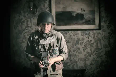 A scene from the movie Lee (2023) featuring Kate Winslet, depicting a soldier in a vintage setting, holding a camera amidst a richly patterned background.